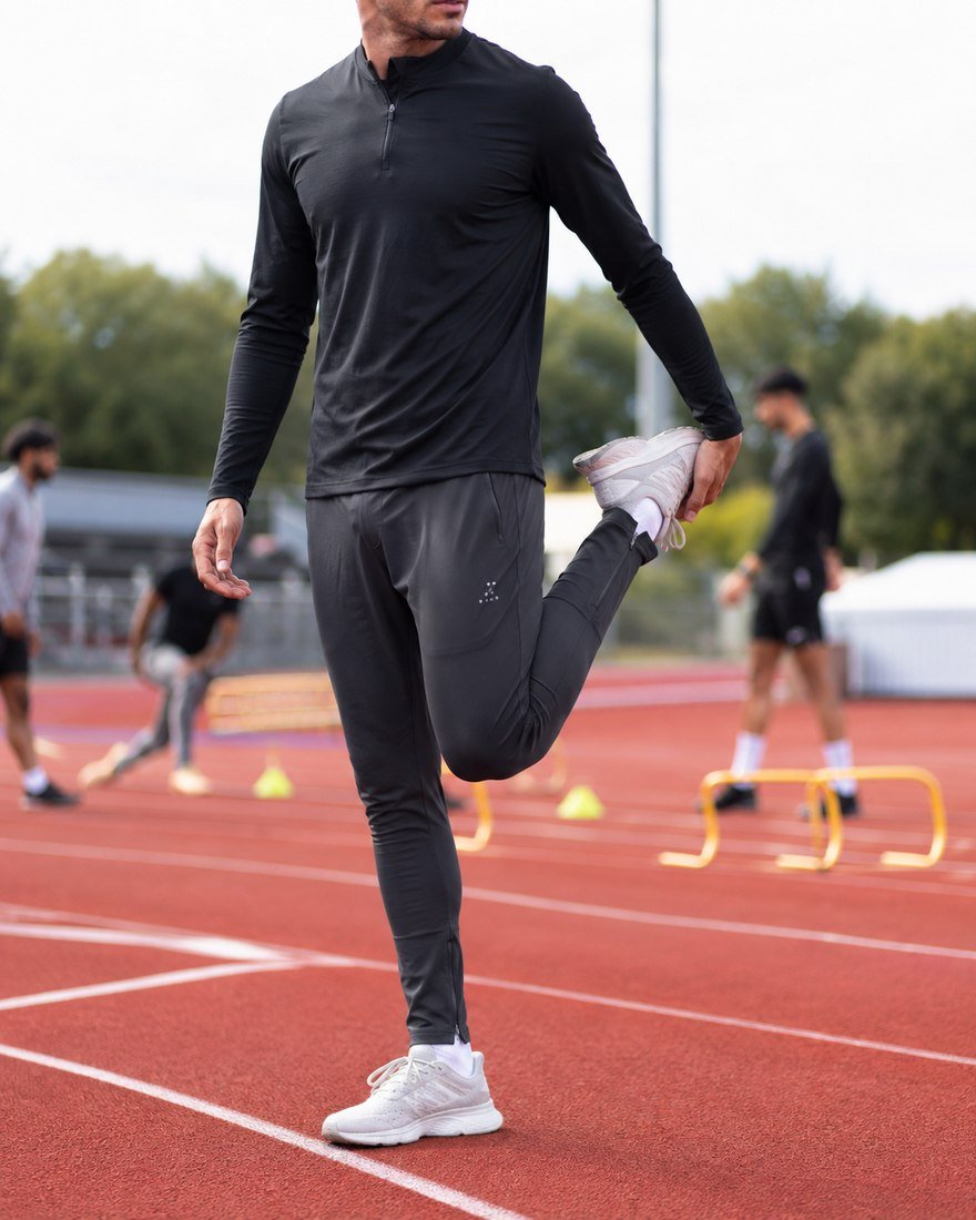 Athlete stretching on a track in grey training bottoms